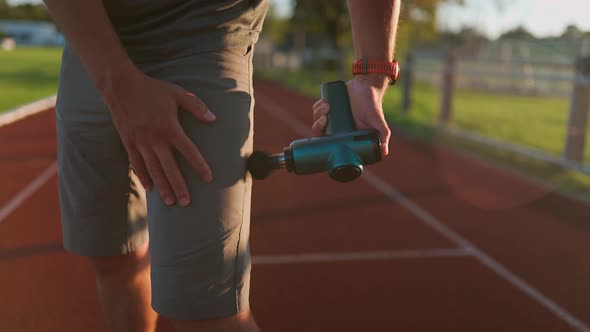 A Male Athlete Massages Muscles and Tendons with a Massage Percussion Device After a Workout at the alt