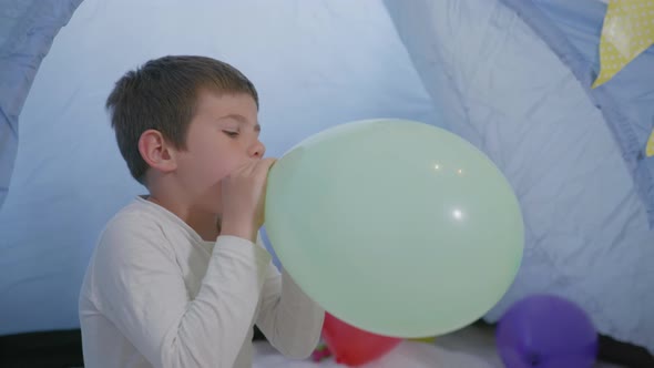 Childrens Leisure, a Handsome Friendly Boy Has Fun Inflates a Balloon Playing in a Wigwam alt