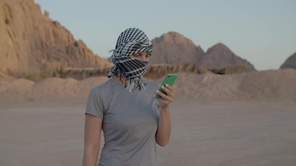 Female Tourist in Checkered Keffiyeh Trying to Find Mobile Network Using Smart Phone Standing in alt