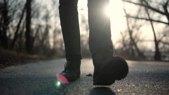 Man Feet Walking On Road At Sunrise. Lonely Walker Guy Rest On Holiday. Man Legs Walking On Park. alt