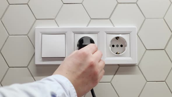 Man Hand Inserts a Plug Into Black Electrical Outlet on White Wall alt
