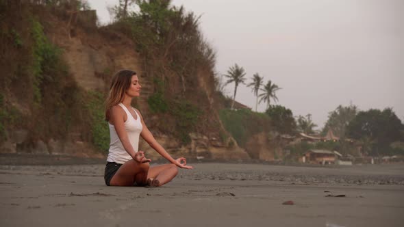 Young Woman Meditating in Lotus Pose on Ocean Shore alt