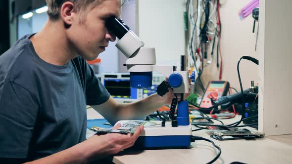 Repair Specialist Looking at System Board Through Microscope alt
