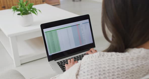 Back view of asian woman sitting on sofa and working remotely from home with laptop alt