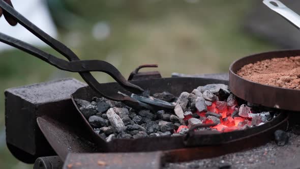 Close-up A blacksmith turns a molten red metal horseshoe over the fire with tongs.