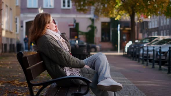 Woman Have a Talk By Smartphone Sitting on the Bench in the Street of Old Town  60p