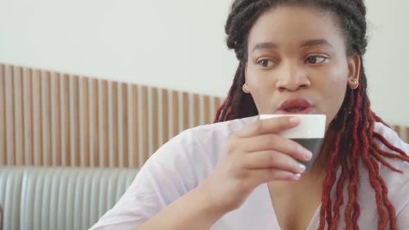Attractive Young African Woman Drinking Cappuccino and Talking in Cafe alt