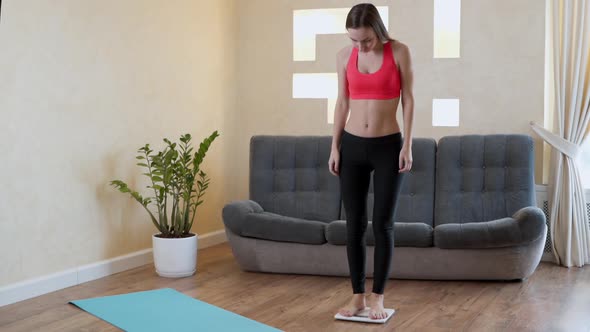 Distressed Woman in Sportswear Measures Her Weight on the Floor Scales alt