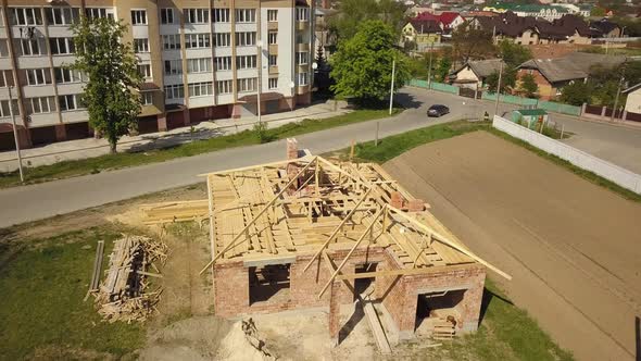 Aerial view of unfinished brick house with wooden roof frame structure under construction. alt