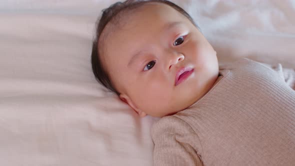An Asian newborn baby is laying down on a soft white sheet mattress. Starring at his parents and fee alt