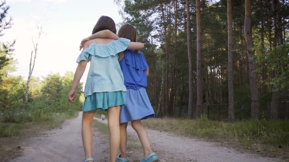 Two Cute Girls Are Walking Along the Forest Road and Talking