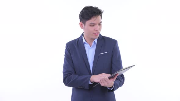Happy Young Asian Businessman Talking While Holding Clipboard alt