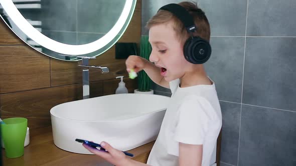 Boy in Headphones Watching Videos on His Phone while Cleaning His Teeth Using Toothbrush alt