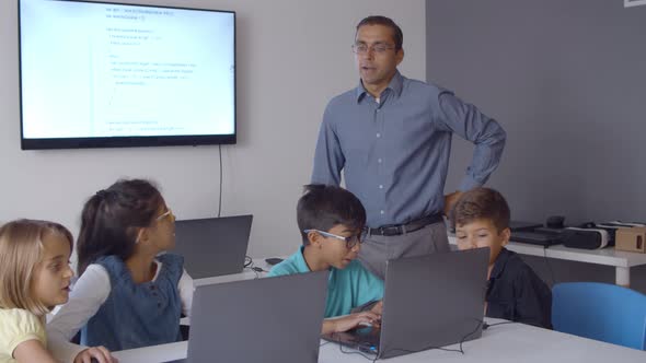 Teacher Watching Excited Classmates Using Laptops alt