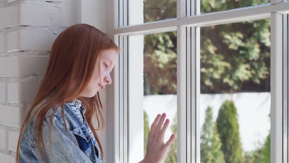 Sad Teen Girl Looking Out Window at Home Isolation