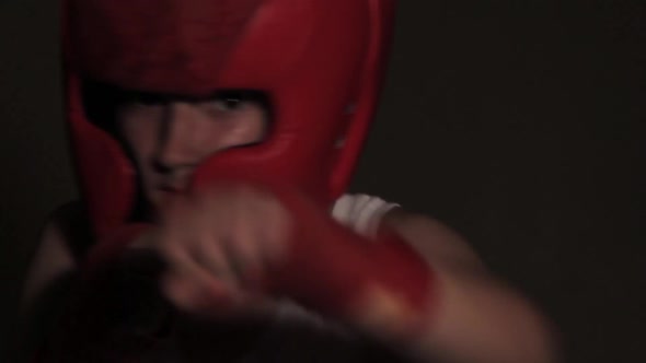 Young guy boxer in a red protective helmet posing at the camera close-up in bandages