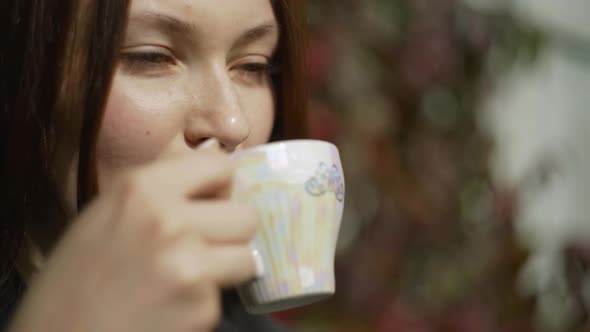 Woman in a Jacket Jeans Sits Near the House Drinks Tea From a Porcelain Glass