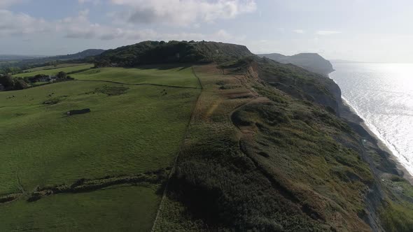 Golden cap and Charmouth beach cliffs are revealed with an aerial track from inland to out to sea lo alt