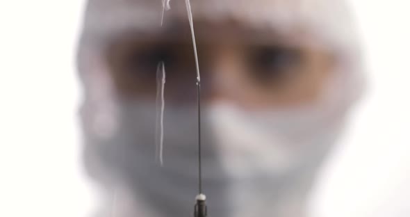 Closeup of Woman in a Protective Suit with a Syringe Looking to a Syringe with Vaccine
