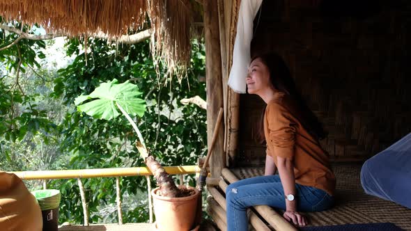 A young asian woman sitting on wooden cabin looking at beautiful view