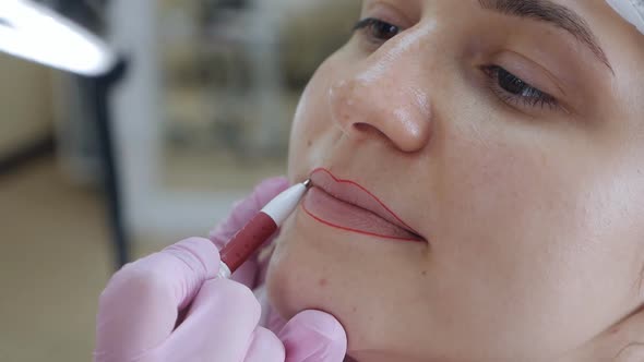 Closeup of a Permanent Makeup Master with a Red Cosmetic Pencil Draws a Contour Sketch of Future