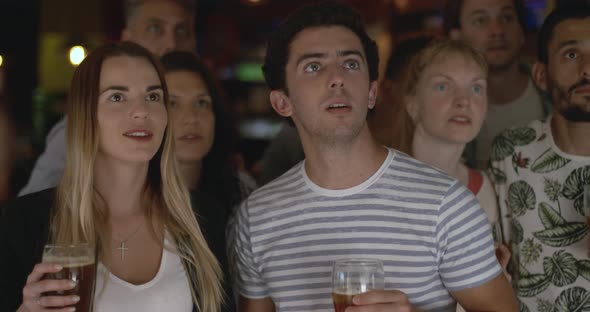 Sports fans cheering while watching televised match in sports bar, slow motion alt