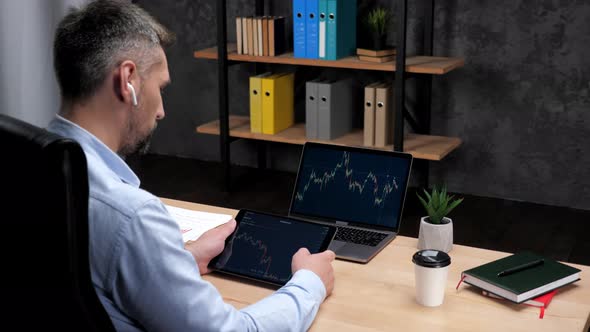 Man Broker Scrolling Tablet with Stock Exchange Chart Laptop with Stock Market alt