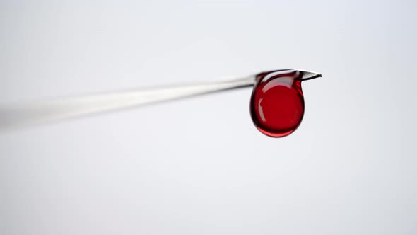 Close-up Red Liquid Dripping From Syringe on White Background alt