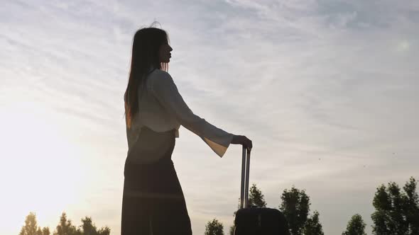 Woman Silhouette Stands with Suitcase at Back Cloudy Sunset alt