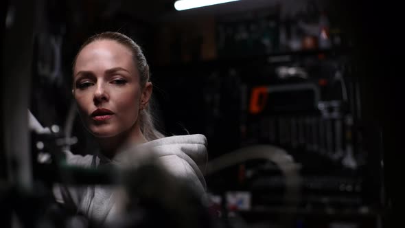 Pretty Female Mechanic Performing Diagnostic and Repairing of Bicycle Working in Dark Garage of alt