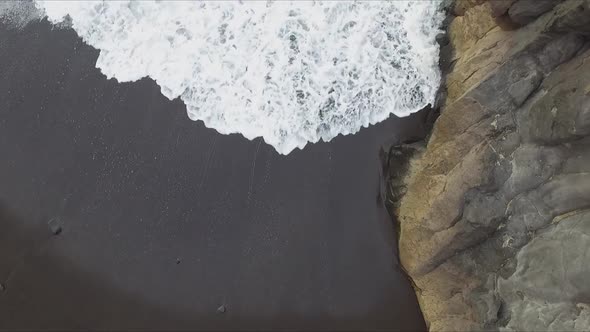 Aerial view of splashes and swashes of waves on cliff rocks at volcanic beach seashore. White foam b alt