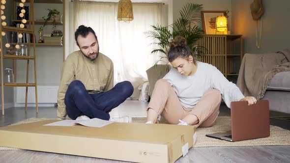 Lovely Couple Looks at Manual To Assemble Furniture on Floor
