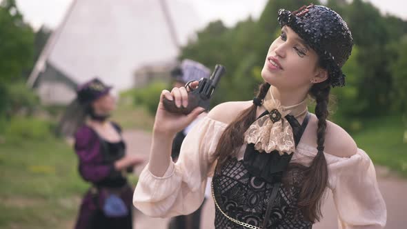 Young Slim Beautiful Woman with Steampunk Makeup in Costume Aiming with Gun Away Smiling and Blowing alt