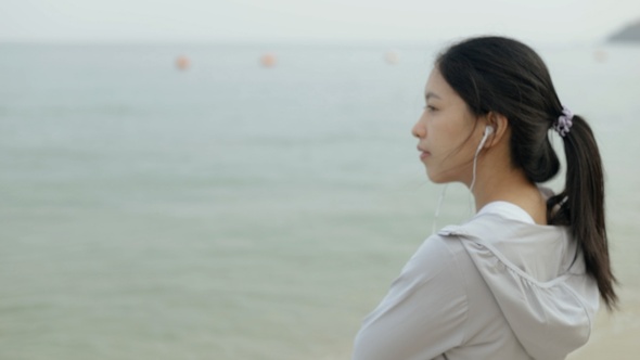 Asian athletic woman wearing sportswear and listening to music looking out at the ocean view.