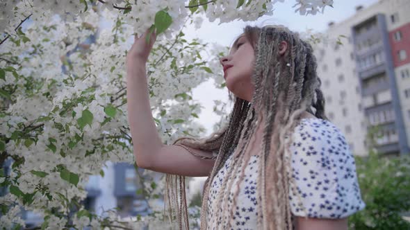 A Cute Girl with Dreadlocks Poses By a Tree with Leaves