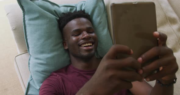 Video of happy african american man lying on sofa and using smartphone alt