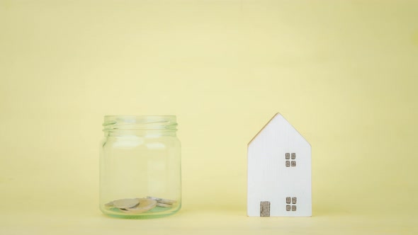 Stop motion animation mini house and coin into a clear glass jar on yellow background.