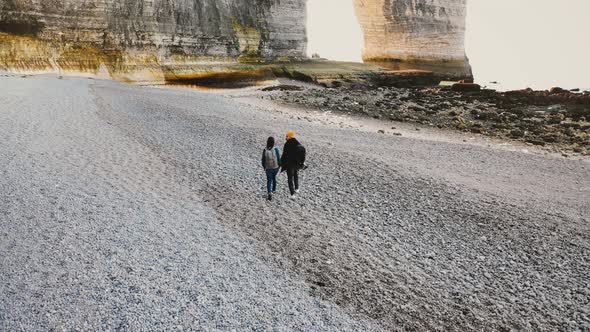 Drone Camera Follows Happy Romantic Tourist Couple Walking Along Amazing Pebble Beach To Epic White alt