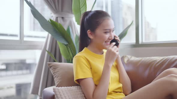 Young Asian woman using smartphone lay on sofa happy and smile. alt
