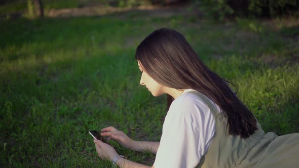 Attractive Woman Relaxing on Grass in Park Using Smartphone Enjoying Summer