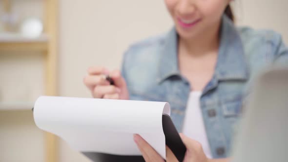 young woman working laptop on desk in living room at home writing notebook document