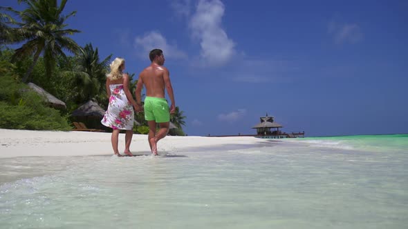 A couple walks on the beach holding hands at a tropical island resort hotel alt