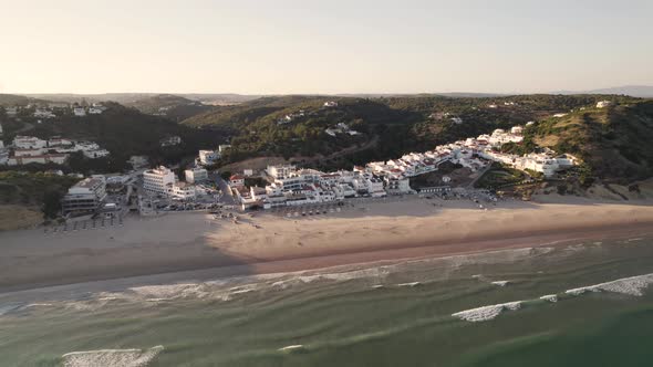 Fast pull back aerial revealing the green backland surrounding the wide beach of Salema, Portugal alt