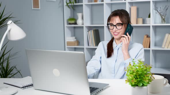 Happy young business woman talking on a cell phone using a laptop.