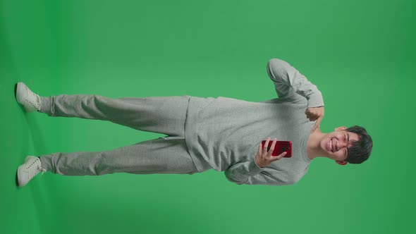 Young Asian Boy Use Mobile Phone And Pointing To Smart Phone While Standing In The Green Screen alt