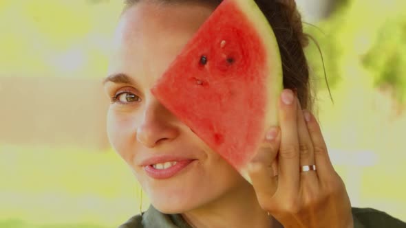 Closeup View at Young Female Smiling and Hiding Behind Slice of Watermelon