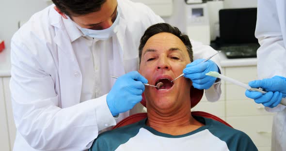 Dentists examining a male patient with tools alt