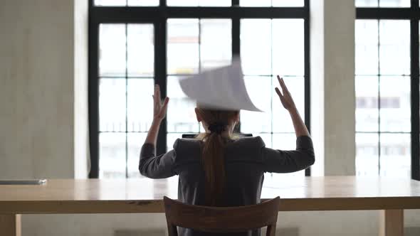 A woman freaks out and throws work papers into the air alt