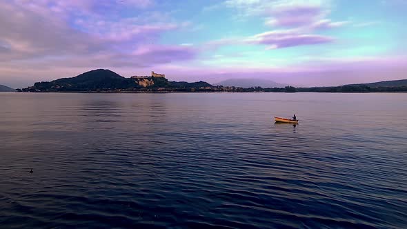 Evocative wide-angle pov of small fishing boat with fisherman rowing in lake waters of Maggiore lake alt