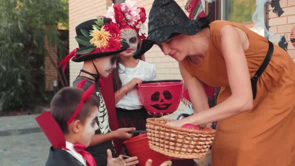 Adorable Children in Halloween Costumes Receiving Candy from Woman alt